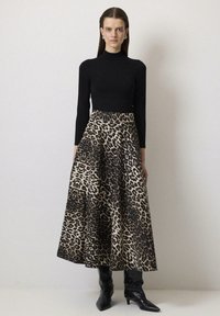 Top nero a maniche lunghe abbinato a una gonna a trapezio con stampa leopardata, dotata di vita alta e pieghe, completato da stivali neri fino al ginocchio.