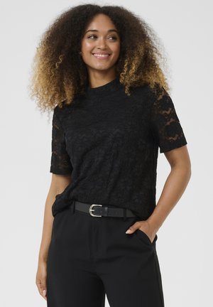 Top in pizzo nero con maniche corte e collo a lupetto, caratterizzato da un motivo floreale. Abbinato a pantaloni neri e una cintura argentata.