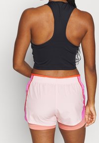 Černý sportovní top s průstřihem na zádech v kombinaci s světle růžovými šortkami s oranžovými a růžovými akcenty po stranách a elastickým pasem.