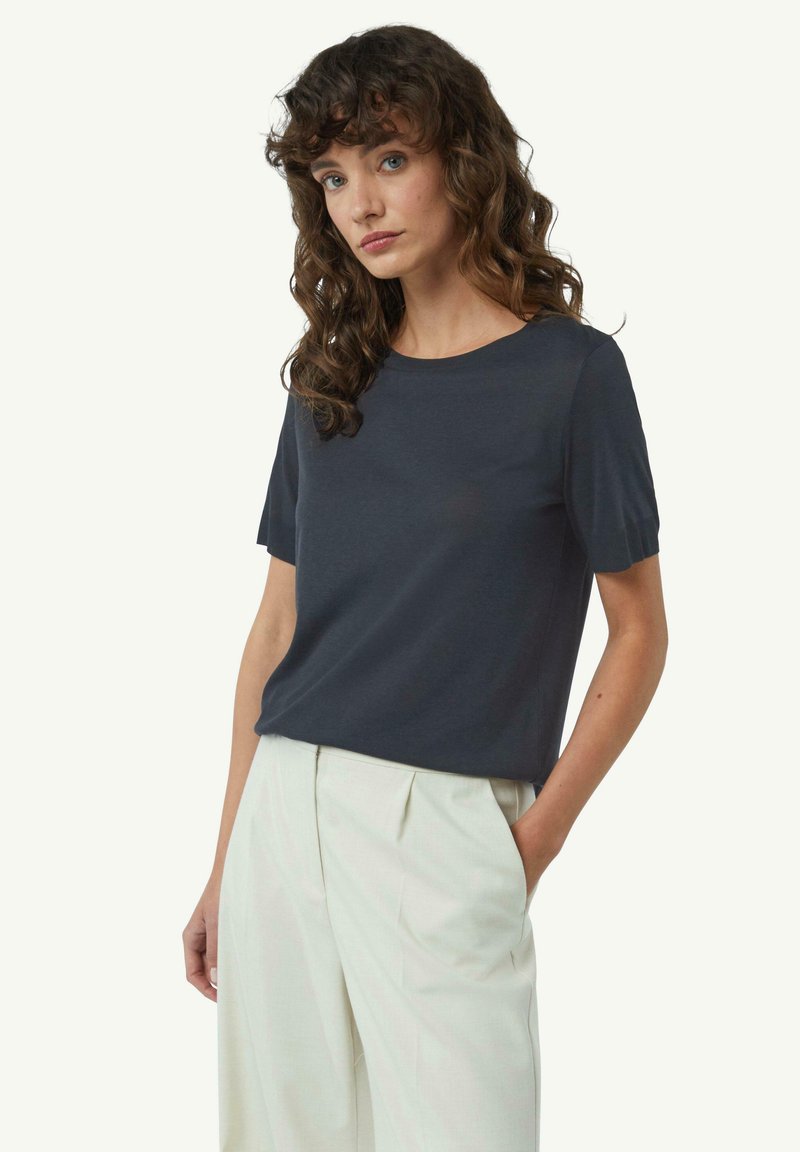 Czarna krótka koszulka z okrągłym dekoltem, wykonana z miękkiego materiału, zestawiona z jasnymi spodniami o wysokim stanie.