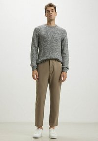 Maglione grigio a coste abbinato a pantaloni beige su misura e sneakers bianche. L'outfit presenta una vestibilità morbida e un design a maglia testurizzata.