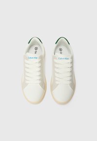 Des baskets blanches au toucher lisse, dotées d'accents gris, de lacets blancs et d'un détail de talon vert ; marquées "Calvin Klein" sur la languette.