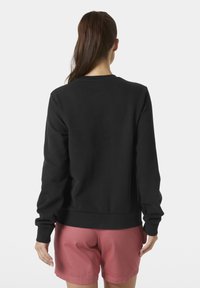 Sudadera negra de manga larga, con puños y dobladillo acanalados. Textura suave, diseño clásico de cuello redondo. Combinada con shorts rosas.