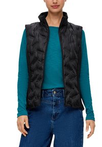 Schwarze gesteppte Weste mit hohem Kragen, mit Reißverschluss, getragen über einem türkisfarbenen Langarmshirt. Eine blaue Jeans rundet das Outfit ab.