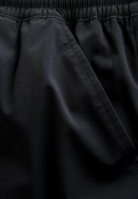 Mustast kangast, millel on sile tekstuur, ja elastse vöökohaga ning kolmnurkse plaastrilise detailiga. Materjal on kerge ja pehme.