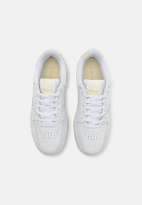 Hvite lær sneakers med mesh-detaljer, rund tå, snøring, perforeringer på sidene og subtile gule akenter.