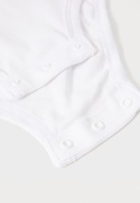 Bodysuit pour bébé en coton blanc à manches courtes, avec des boutons-pression en bas et une couture délicate le long des bords.