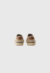Beige kanvas espadrilles med brune læderdetaljer, synlig søm og vævede jutesåler. Rundet bagside-design og mørke trimdetaljer.