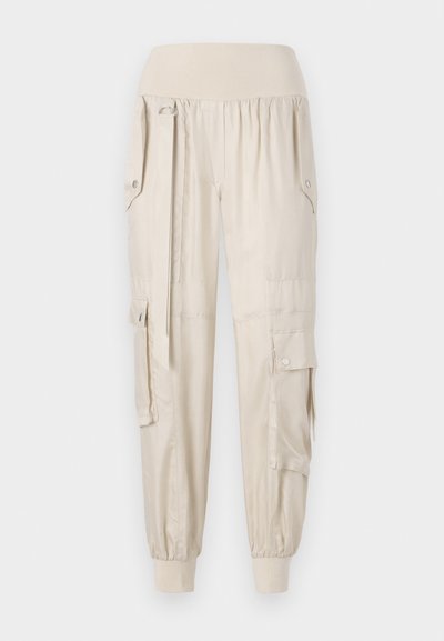 Beige Cargo-Hosen mit elastischem Bund, schmal zulaufenden Bündchen, Seitentaschen und Knopfdetails. Aus leichtem Stoff mit glatter Textur gefertigt.