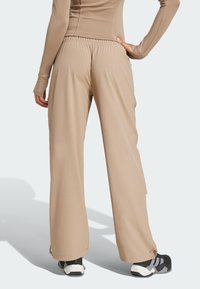 Beżowe szerokie spodnie z elastycznym pasem, o gładkiej fakturze i regulowanych nogawkach. Noszone z czarno-białymi sneakersami.