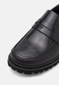 Svarta läderloafers med en slät finish, med en stilren plastaccentband och en hållbar gummisula med distinkta mönster.