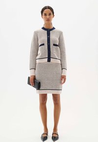 Knit two-piece set featuring a cream cardigan with navy accents and buttons, paired with a matching knee-length skirt and black clutch.