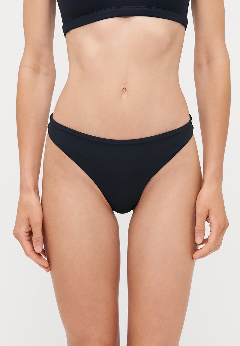 Svart bikiniunderdel med låg midja, släta kanter och minimal täckning. Tillverkad av stretchigt tyg med matt yta.
