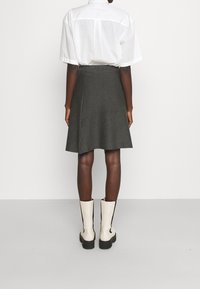 Falda acampanada gris de tela, combinada con una camisa blanca a rayas y botas blancas hasta la rodilla con detalles negros.