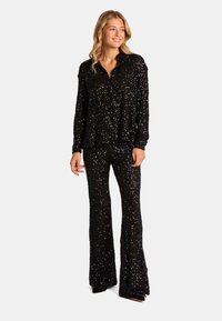 Conjunto de top negro con lentejuelas y pantalones acampanados, que presenta un diseño de camisa con cuello y una superficie brillante y texturizada que refleja la luz.