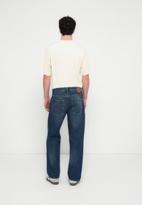 Helebeež lühikeste varrukatega soonikkoeline särk, kantud tumelõhnavate laia lõikega teksadega, millel on nahast plaastriga ja kaks tagataskut.