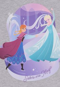 Grafika przedstawiająca dwie animowane postacie, jedną w niebieskiej sukience, a drugą w fioletowej sukience, ze śnieżynkami i napisem "Siostry to magia."