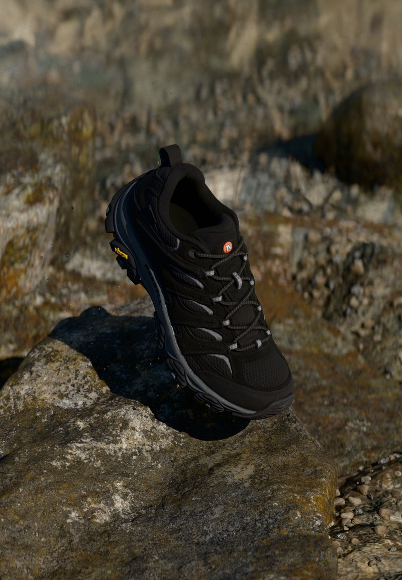 Black hiking shoe with a mesh upper and rubber sole, highlighted by gray accents and a yellow logo, placed on a rocky surface.