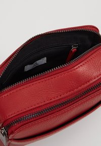 Punainen nahkalaukku, jossa on sileä pinta, vetoketjullinen avaus, sisätasku ja kontrastivärinen musta kangasvuori.