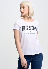 Bílý tričko s krátkým rukávem s potiskem "BIG STAR" v tmavě modré barvě. Volný střih, kulatý výstřih a měkká bavlněná textura. V kombinaci s modrými džíny.