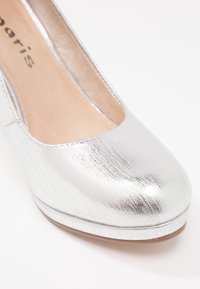 Chaussure compensée fermée en cuir argenté texturé avec doublure intérieure beige et détails de couture subtils le long des bords.