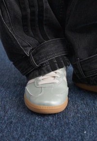 Svijetloplave, sjajne tenisice s bijelim detaljima i gumenenim smeškastim đonom. Nosite ih uz crne, ležerne traperice s preklopnim rubom.