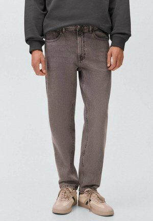 Uomo che indossa jeans dritti grigi sbiaditi, sneakers beige con strisce scure e un felpa grigio scuro, in piedi su uno sfondo neutro.