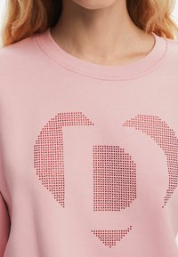 Różowa bluza z okrągłym dekoltem i fakturowaną powierzchnią ozdobioną wzorem czerwonych kropek tworzących stylizowany grafikę.