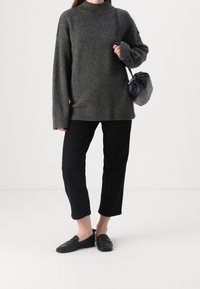 Grijze oversized gebreide trui met een hoge hals, gecombineerd met zwarte cropped broek en zwarte loafers. Een kleine zwarte tas maakt de outfit compleet.
