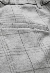 Grått tyg med ett subtilt rutig mönster, med en bakficka och kontrasterande söm längs kanterna. Mjuk textur med en slät finish.