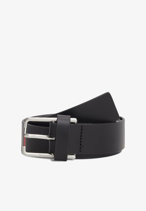 Ceinture en cuir noir roulée avec une boucle rectangulaire argentée comportant un petit détail de logo rouge, blanc et bleu.