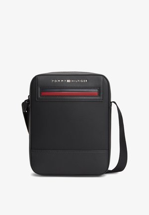 Schwarze Tommy Hilfiger Umhängetasche mit strukturierter Vorderseite, roten und marineblauen Streifen sowie verstellbarem Schulterriemen.