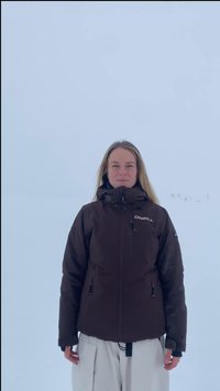 Femme aux longs cheveux blonds portant une veste noire O’Neill et un pantalon blanc, debout dans un décor extérieur enneigé et brumeux.