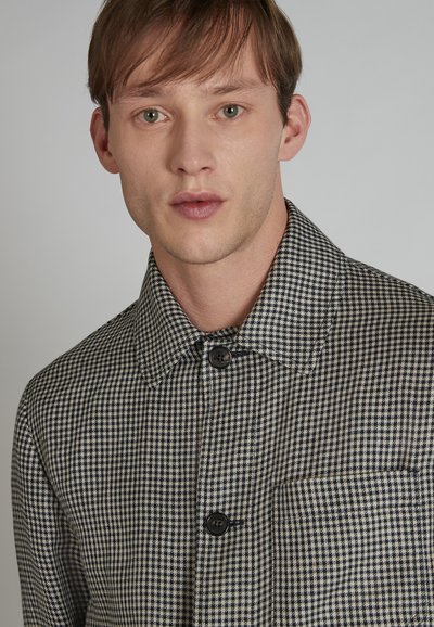 Wzorzysty czarno-biały kraciasty żakiet z kołnierzem, zapięciem na guziki oraz kieszenią po lewej stronie. Teksturowany materiał.