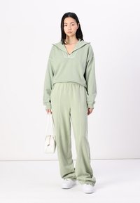 Lys grønn hettegenser med half-zip krage, sammen med matchende løstsittende bukser. Myk stoff med sidepiping-detaljer.