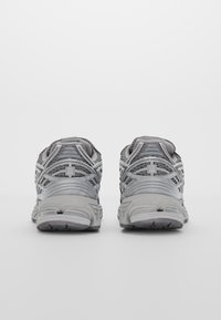 Szürke sportcipők, hálós felső résszel, megerősített burkolatokkal, párnázott sarokkal és texturált gumitalppal. A hátsó nézet kiemeli a tervezési részleteket.