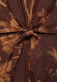 Tissu marron avec un nœud noué présentant un motif de feuille de palmier tropical dans des nuances de brun plus clair.