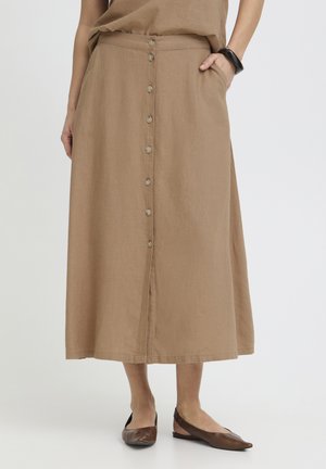 Femme portant une jupe midi beige boutonnée devant avec des poches et des ballerines pointues marron, debout devant un fond clair.