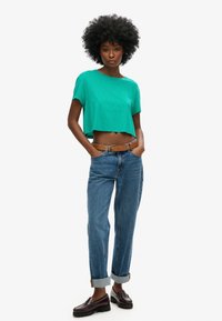 Grøn cropped t-shirt lavet af blødt stof, parret med højtaljede blå denimjeans, der er rullet op ved manchetterne, og mørke loafers med kraftige såler.