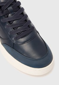 Dunkelblaue Sneaker mit Stoffsenkeln, Obermaterial aus Leder, Veloursleder-Zehenschutz und weißer Gummisohle auf hellem Hintergrund.