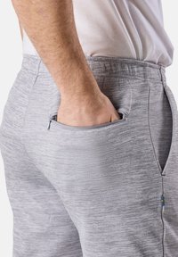 Graue Sporthose mit strukturierter Oberfläche, ausgestattet mit einer Reißverschlusstasche an der Seite und einem elastischen Bund für zusätzlichen Komfort.