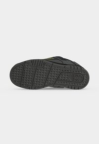 Semelle de basket noire avec motif texturé antidérapant et logo embossé sur un fond uni, montrant le dessin de la bande de roulement et les détails de la base de la chaussure.