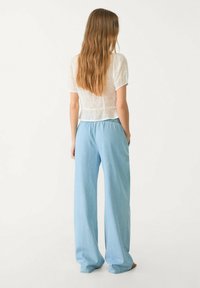Blouse blanche légère et transparente avec détail en broderie anglaise, associée à un pantalon large en denim bleu clair. Texture douce, coupe décontractée.