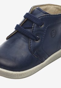 Zapato de cuero azul marino con punta redondeada, diseño de cordones, lengüeta texturizada y suela de goma blanca con pequeñas manchas claras. Detalle del logo en el lateral.