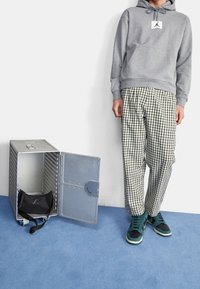 Sweat à capuche gris, pantalon à carreaux noir et blanc, baskets bleu sarcelle et noir ; conteneur de rangement métallique avec un sac noir à l'intérieur.