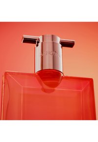 Primo piano di un flacone di profumo rettangolare rosso con una spruzzatore argentato inciso con il nome del marchio Lancôme.