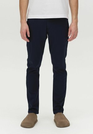 Navy blue trousers made of stretch fabric, featuring a slim fit design, front pockets, and a smooth texture. Paired with brown slip-on shoes.
