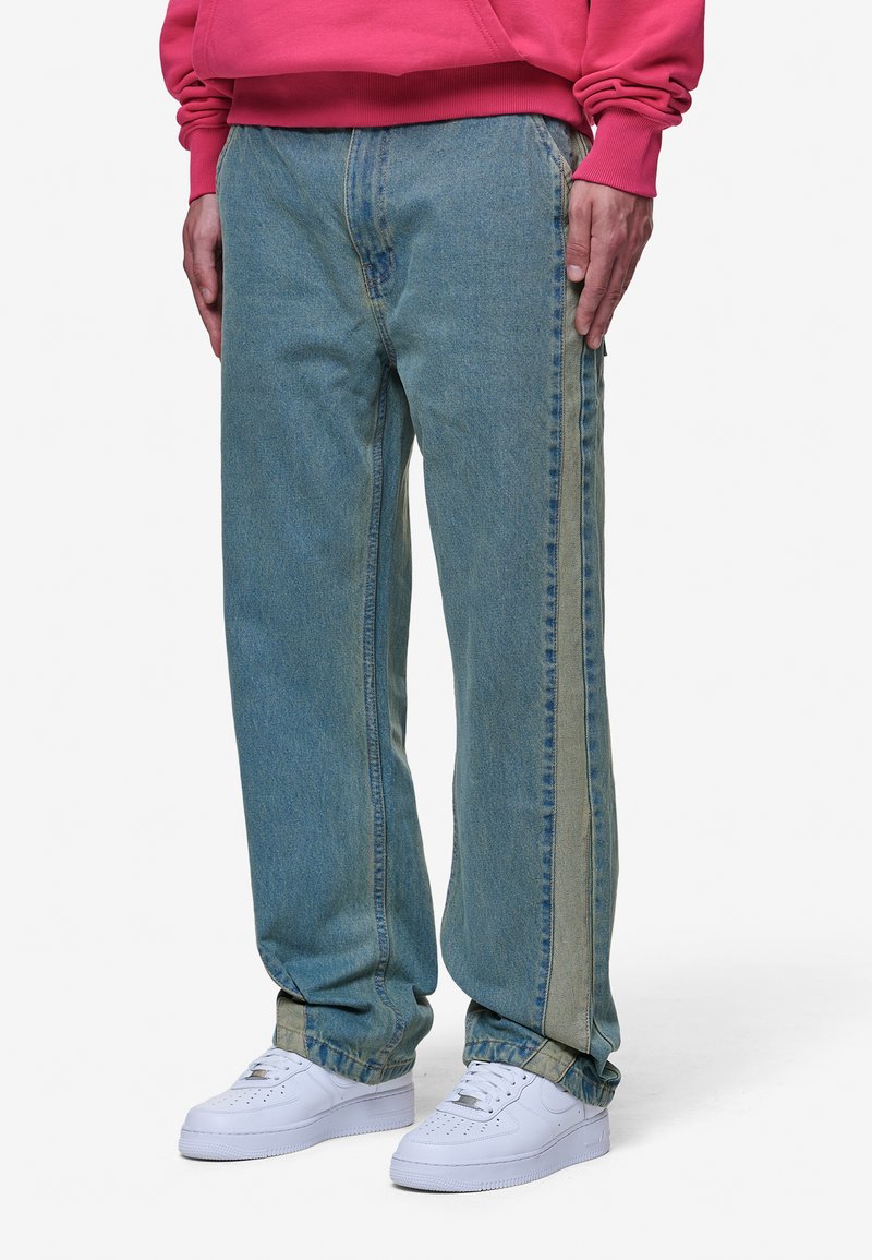 Gaišzilas džinsi ar brīvu piegriezumu un kontrastējošu vertikālu svītru gar sāniem. Apvienoti ar baltām kedām.