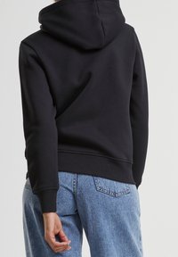 Czarna bluza z kapturem z prążkowanymi ściągaczami na mankietach i dole, zestawiona z jasnoniebieskimi jeansami z tylnymi kieszeniami i luźnym krojem.