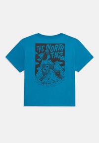 Modra bombažna majica s grafičnim dizajnom na hrbtni strani, ki prikazuje gore, oblake in besedilo "THE NORTH FACE" v črni barvi.